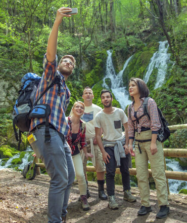 group of friends having fun and taking selfies in front of a waterfall